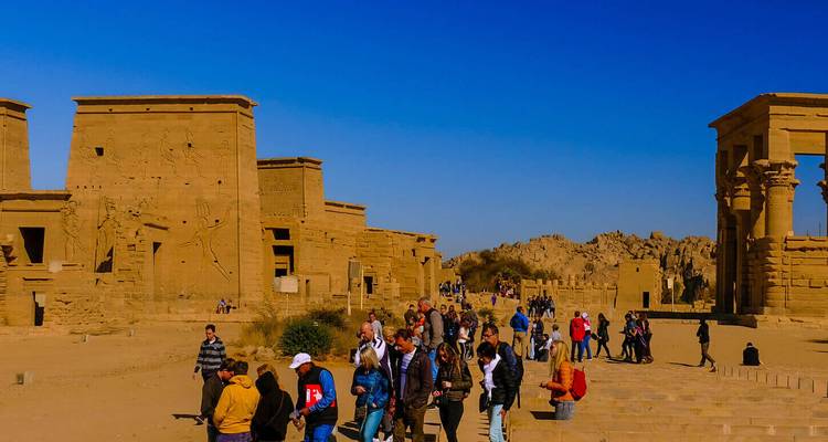 Groupe de touristes explorant le complexe du temple de Philae sous un ciel bleu profond.