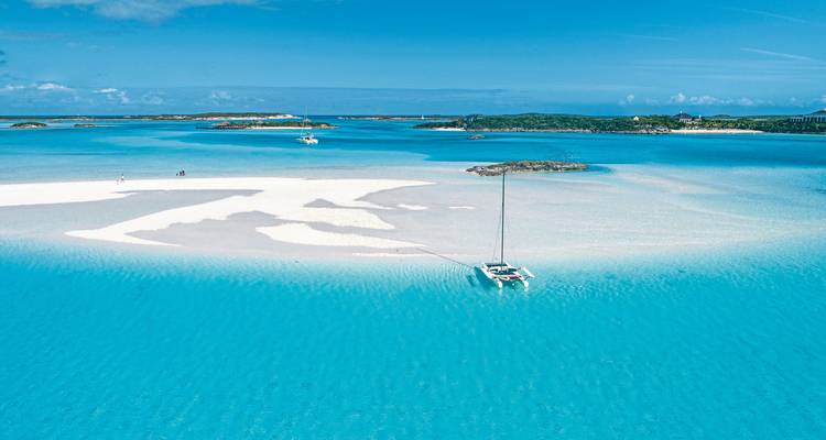Vue aérienne d'une baie bleu clair avec des bancs de sable et un catamaran.