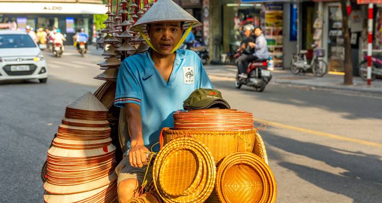 Vendedor callejero en bicicleta cargada de sombreros cónicos tradicionales en Hanoi