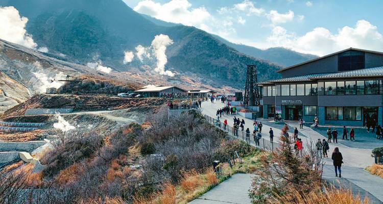 Touristes explorant une zone montagneuse avec des évents de vapeur et des bâtiments.