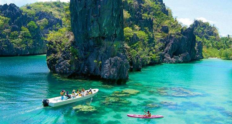 Tourists on a boat and kayak exploring turquoise waters and limestone formations.