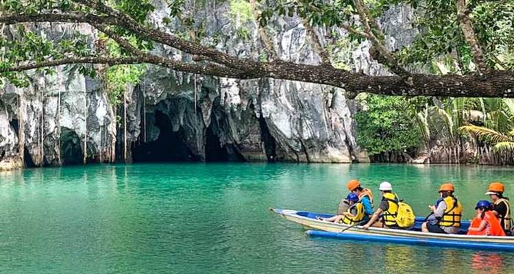 Des touristes avec des gilets de sauvetage dans un bateau sur une voie navigable verte avec des grottes.