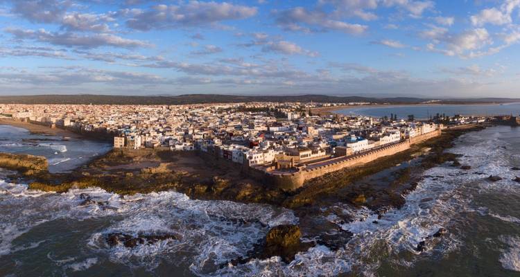 Panorama aéreo de la península fortificada de Essaouira y su costa escarpada bajo la suave luz del atardecer.