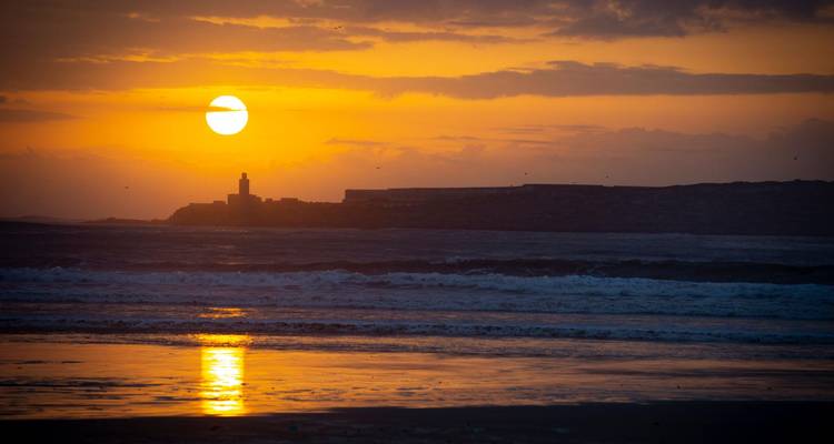 Espectacular puesta de sol sobre las olas del Atlántico con la silueta del fuerte de Essaouira y su reflejo dorado.