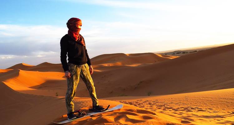 Un solo practicante de sandboard se prepara en lo alto de las dunas naranjas brillantes bajo la suave luz del atardecer.
