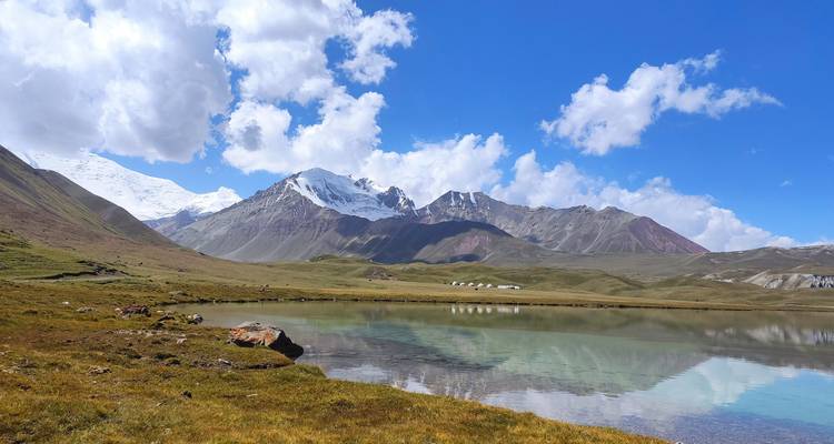 Chaîne de montagnes avec un lac bleu et des berges herbeuses, sous un ciel dégagé.