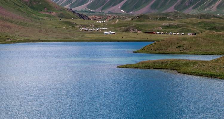Vue sur le lac avec des tentes et des montagnes au loin.