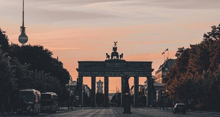 Brandenburg Gate silhouetted at sunset with the Fernsehturm in the background.