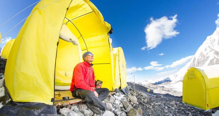 Personne se relaxant devant une tente jaune avec des montagnes autour.