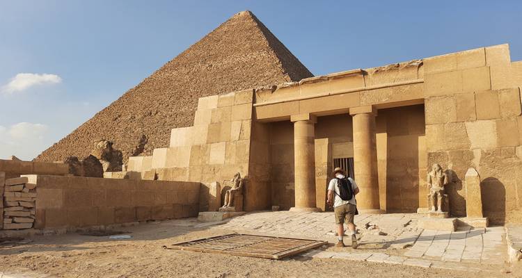 Persoon die staat aan de voet van een piramide met een oude ingang.