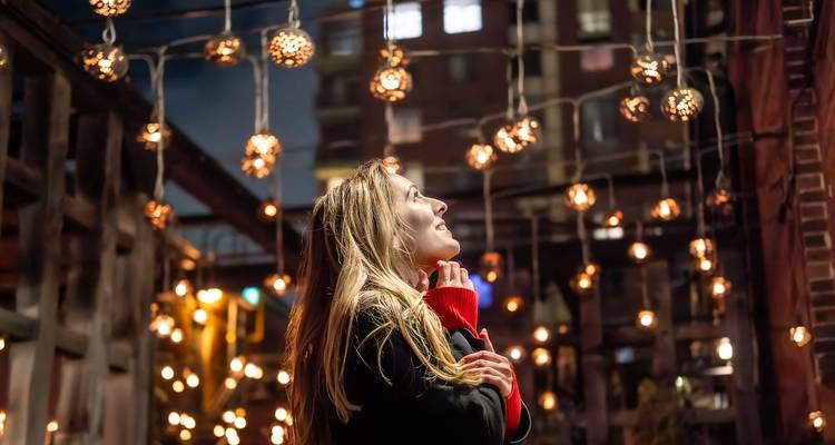 Femme regardant vers le haut des guirlandes lumineuses festives suspendues au-dessus d'elle dans un environnement urbain.