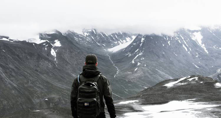 Person gazing at snow-capped mountains under a cloudy sky.