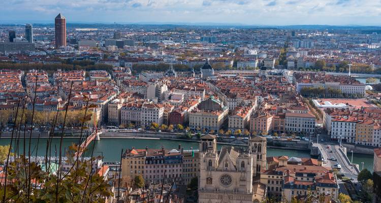 Expansive view of Lyon with the Saône River, red rooftops and city skyline stretching to the horizon.