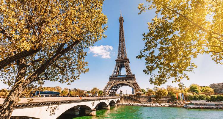 Eiffel Tower rises above the Seine and a graceful bridge framed by autumn foliage.