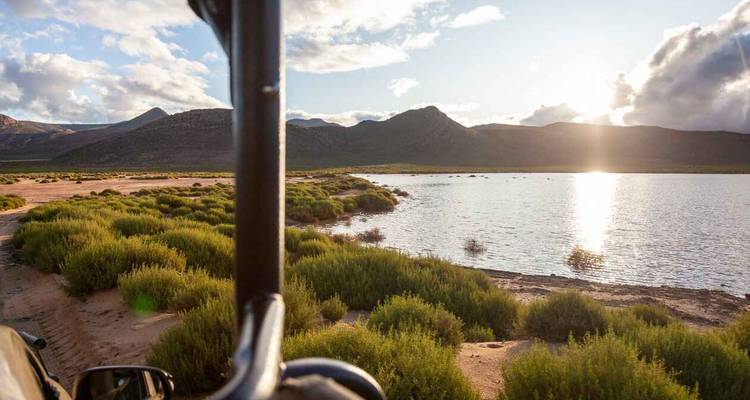 Vue depuis une Jeep surplombant un lac avec des montagnes au loin.