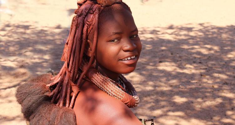 A woman with traditional Himba attire and hairstyle smiling.