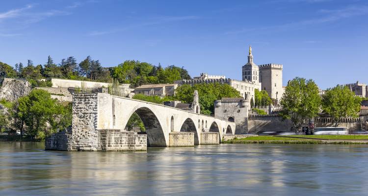Historical bridge over a river with a chateau in the background under clear skies.
