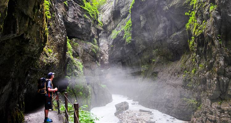 Person standing near a misty gorge with steep cliffs.