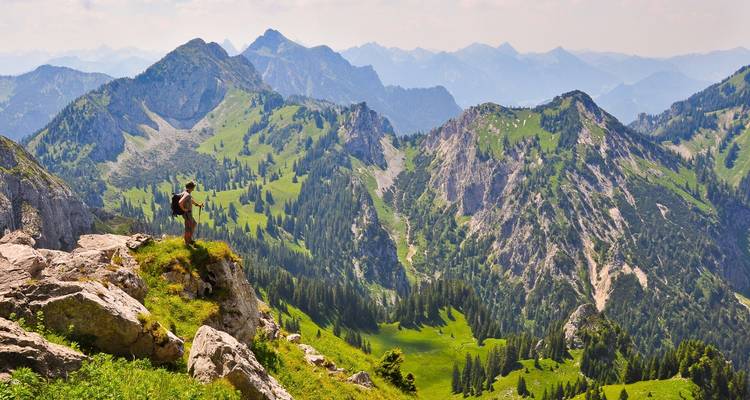 Hiker with a view of green valleys and mountain peaks.