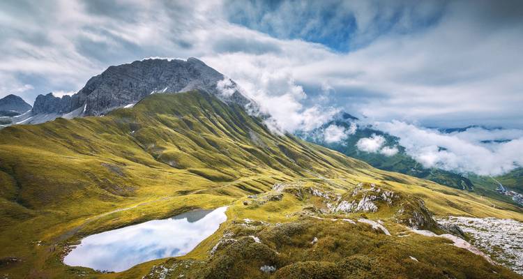 Berglandschaft mit einem spiegelnden See unter bewölktem Himmel.