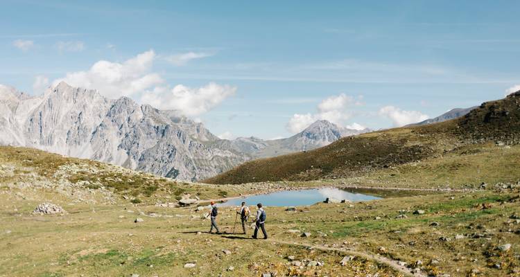 Wanderer überqueren eine Alpenlandschaft mit einem spiegelnden Teich.
