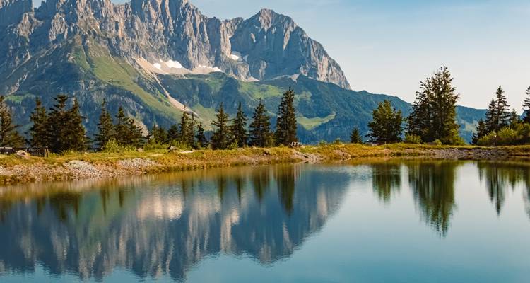 Berge spiegeln sich in einem ruhigen See wider, der von Bäumen umgeben ist.