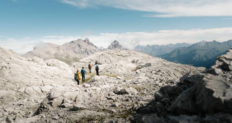 Wanderer, die auf einer felsigen Berglandschaft mit entfernten Gipfeln gehen.