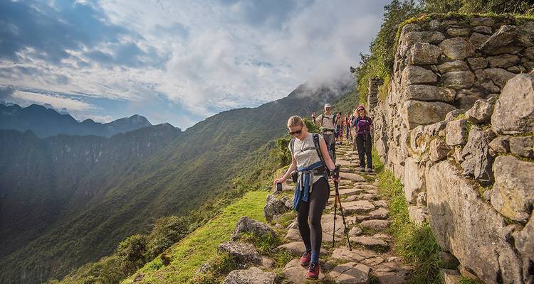 Turistas caminando por un sendero de piedra antigua rodeado de montañas.
