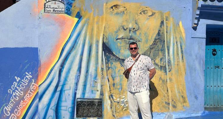 Man posing in front of a mural in a blue-themed street.