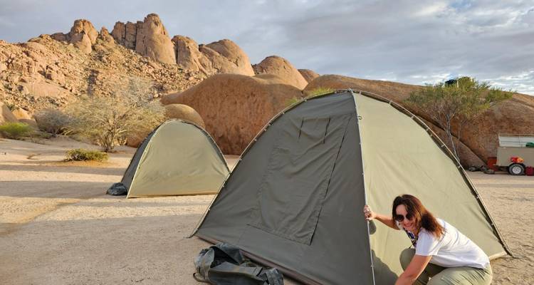 Personne installant une tente dans un paysage désertique rocheux.