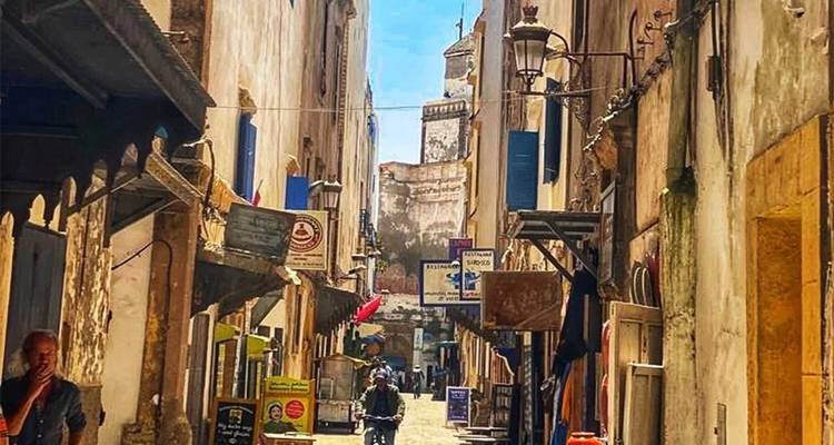 Vue d'une rue étroite avec une architecture traditionnelle et quelques personnes qui marchent.