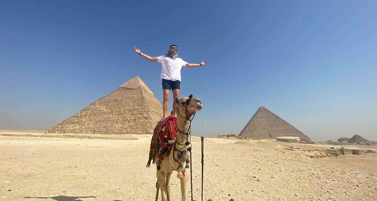 Personne debout sur un chameau devant les pyramides.