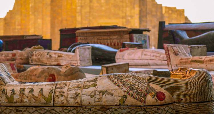 Des sarcophages égyptiens antiques peints et dorés reposant à l'air libre près des ruines de pyramides.