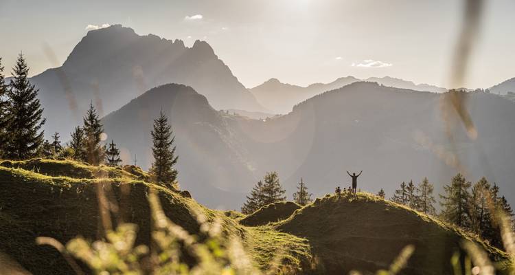 Silhouette d'une personne aux bras levés sur une colline au lever du soleil au-dessus des montagnes.