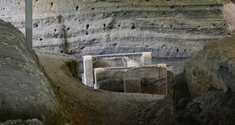 Site de fouille archéologique avec ruines antiques et murs d'enceinte.