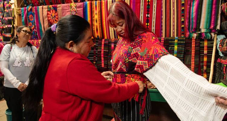 Femmes discutant de tissu dans un marché textile coloré.