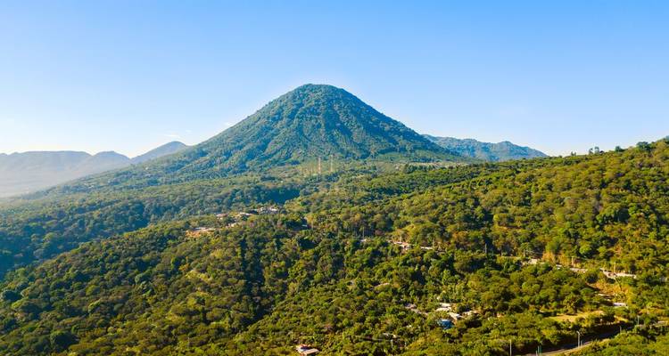 Volcan entouré d'une forêt verte avec un ciel bleu clair.