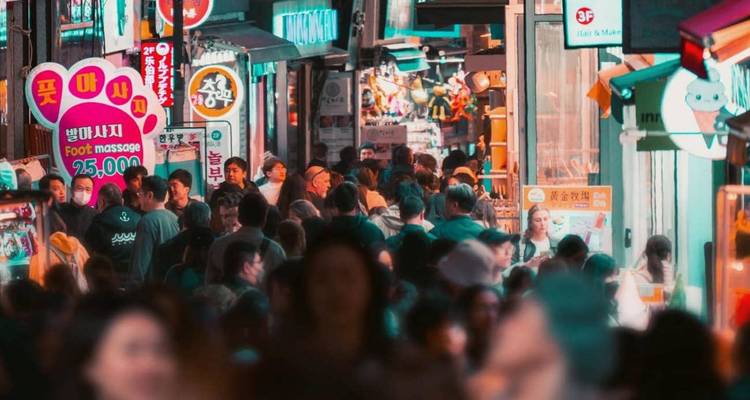Crowded night market alley in Seoul filled with colorful Korean signs and bright shop lights.