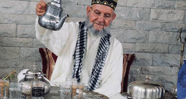 Hombre mayor sirviendo té en un entorno tradicional con teteras de plata.