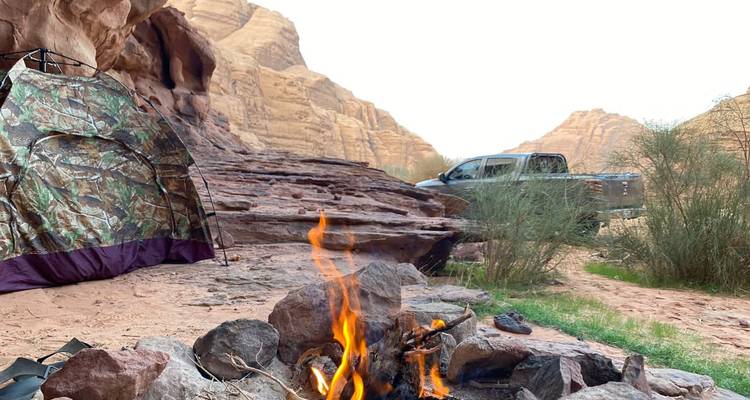 Un camping avec une tente, un feu et un camion dans un décor de désert rocheux.