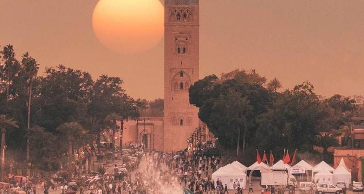 Drukke marktstraat met een moskeetoren en ondergaande zon.