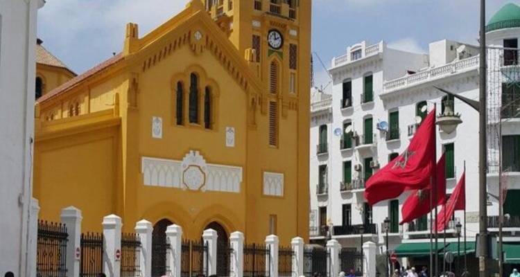 Geel kerkgebouw met een klokkentoren en Marokkaanse vlaggen.