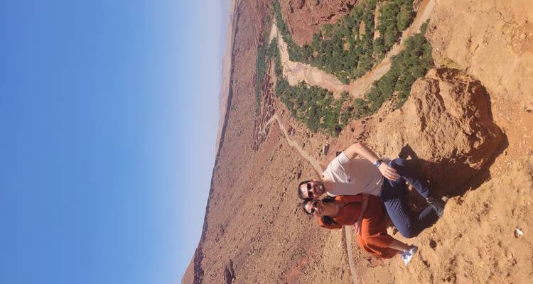 Pareja posando en una roca con un río y paisaje desértico.