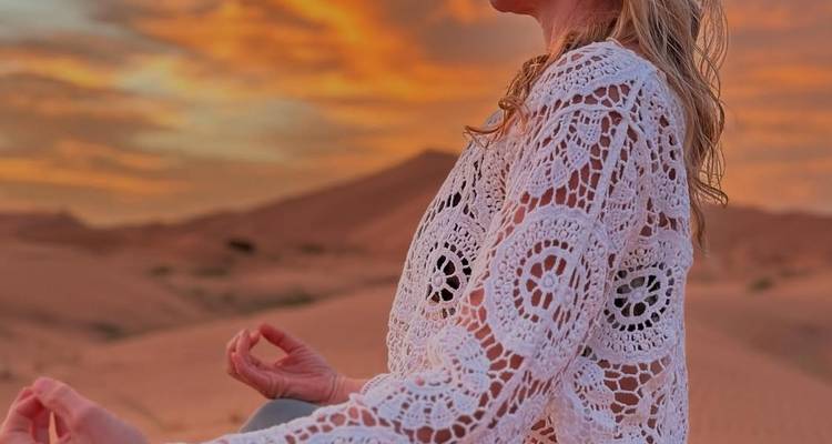 Persona meditando en el desierto con un fondo de atardecer dramático