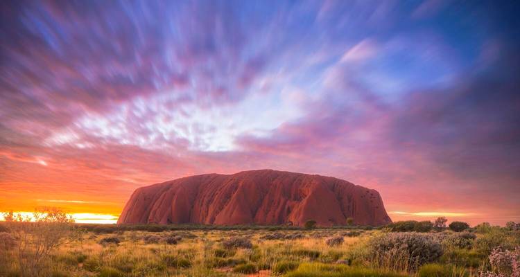 Uluru at dawn with dramatic clouds in the sky.