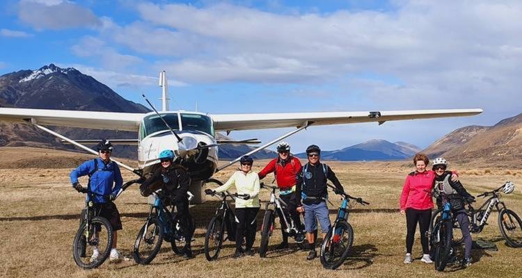 Group of people with bicycles near a small aircraft in a mountainous area.
