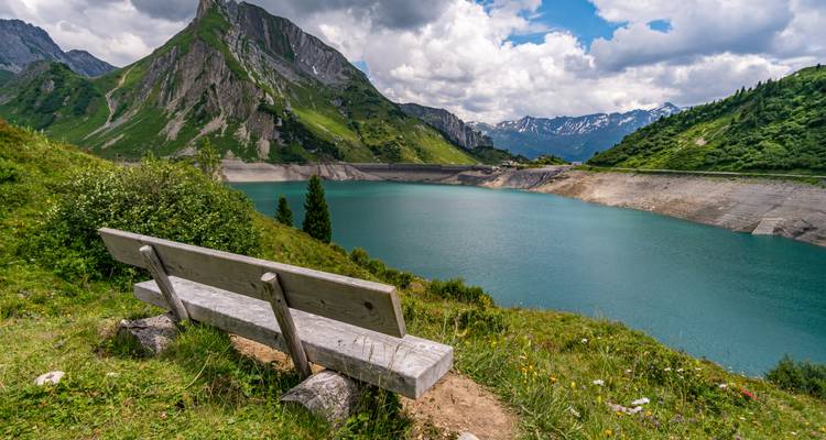 Eine Bank mit Blick auf einen türkisfarbenen See in den Bergen.