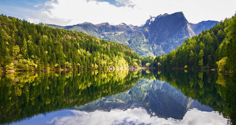 Ruhiger See, der die umgebenden Berge unter einem bewölkten Himmel widerspiegelt.