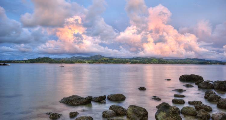 Plan d'eau serein reflétant les nuages au coucher du soleil avec un arrière-plan montagneux.