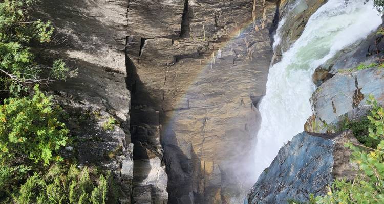 Nahaufnahme eines Wasserfalls mit einem sichtbaren Regenbogen und felsiger Kulisse.